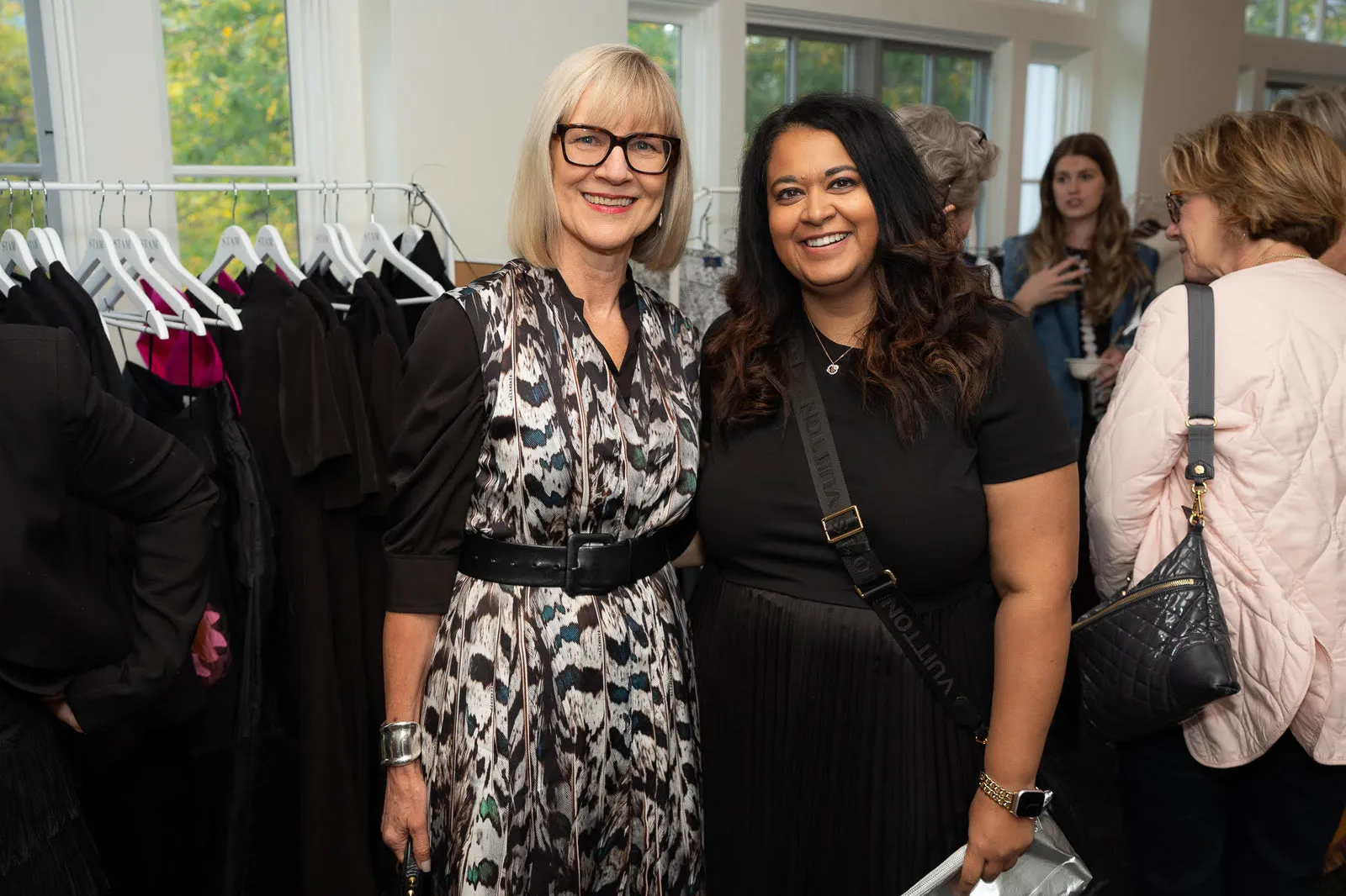 Two guests smiling in front of the clothing racks