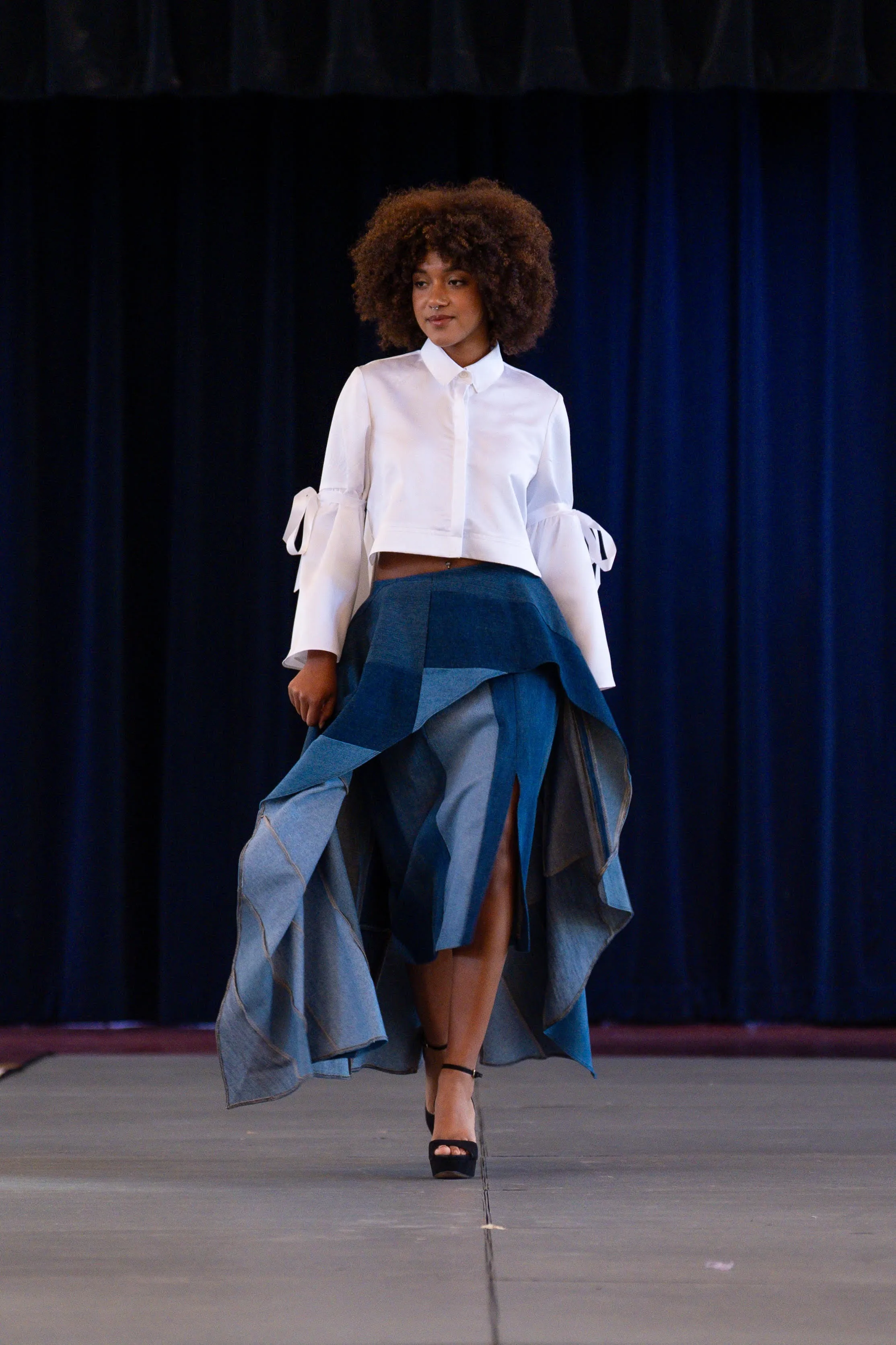 A model in a white blouse and patchwork denim skirt on the runway