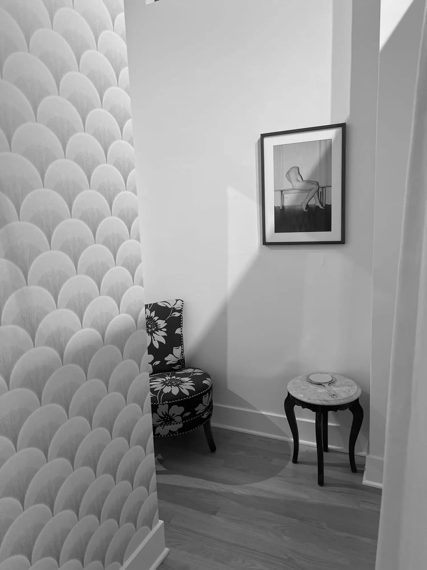 Black and white: a quiet corner of the shop, with scalloped wallpaper, a floral armchair and a framed print above a marble side table
