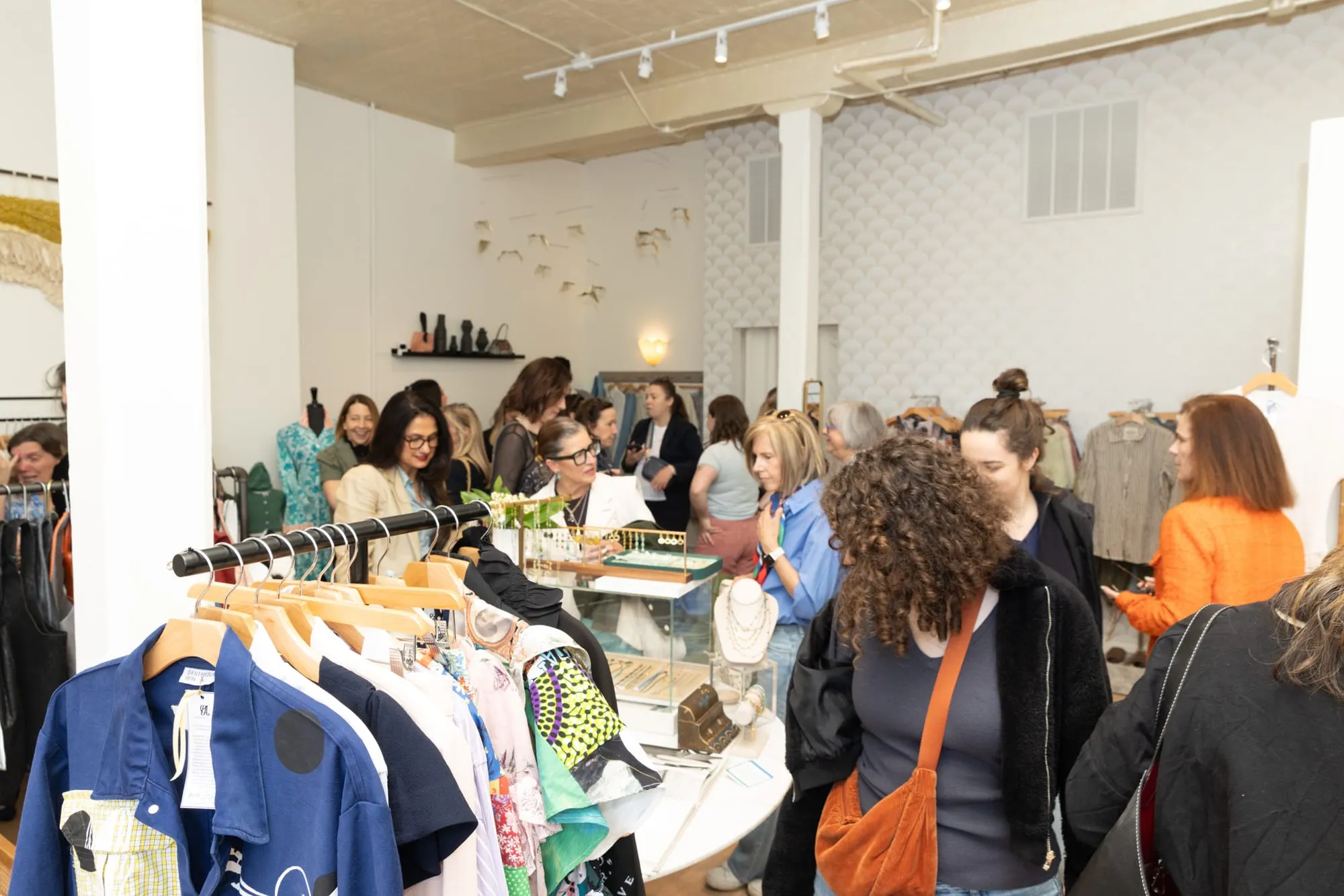 The shop floor full of guests on opening night, talking around the racks and the jewelry case