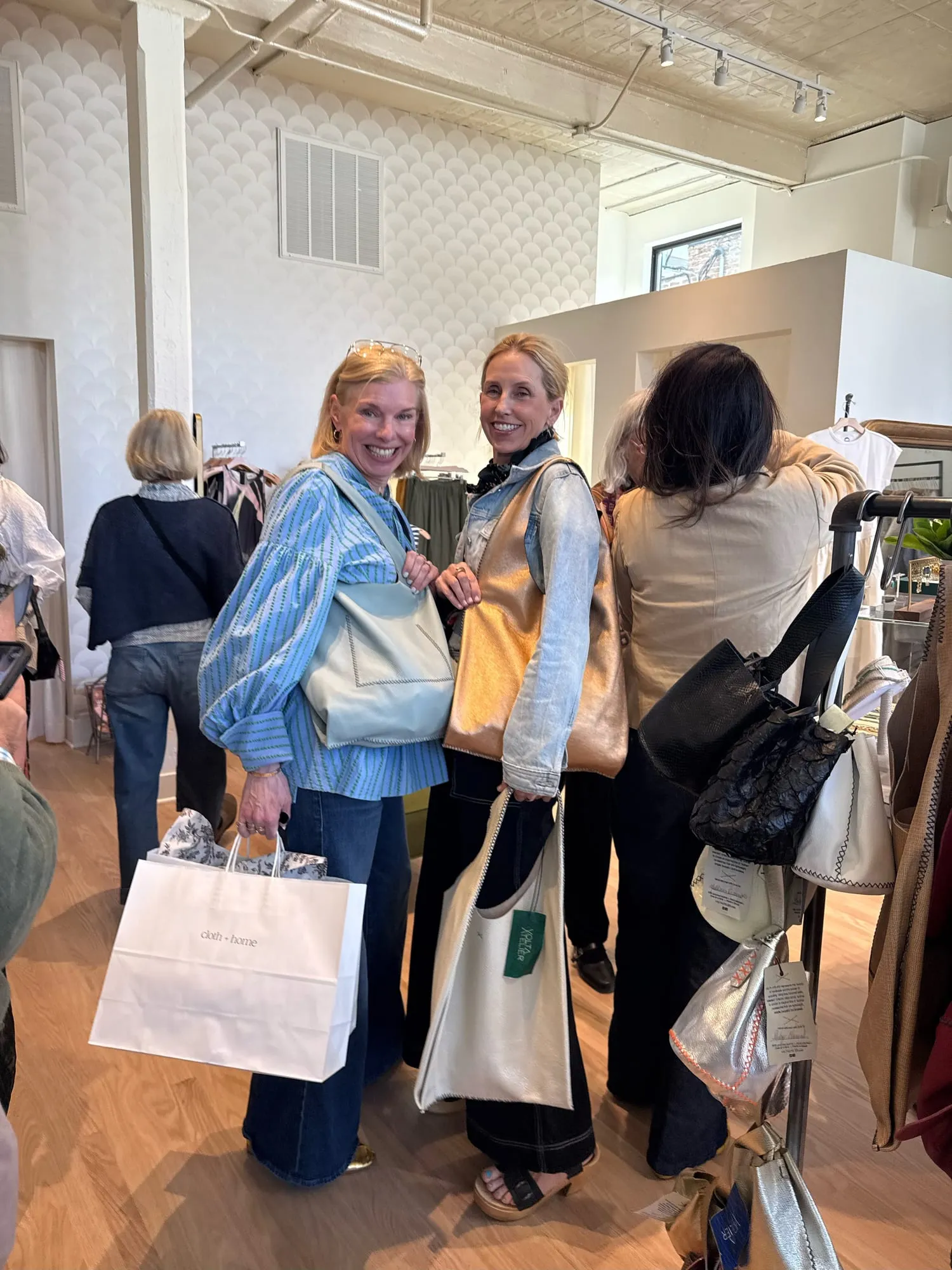 Three customers between the racks carrying tote bags and a wrapped purchase