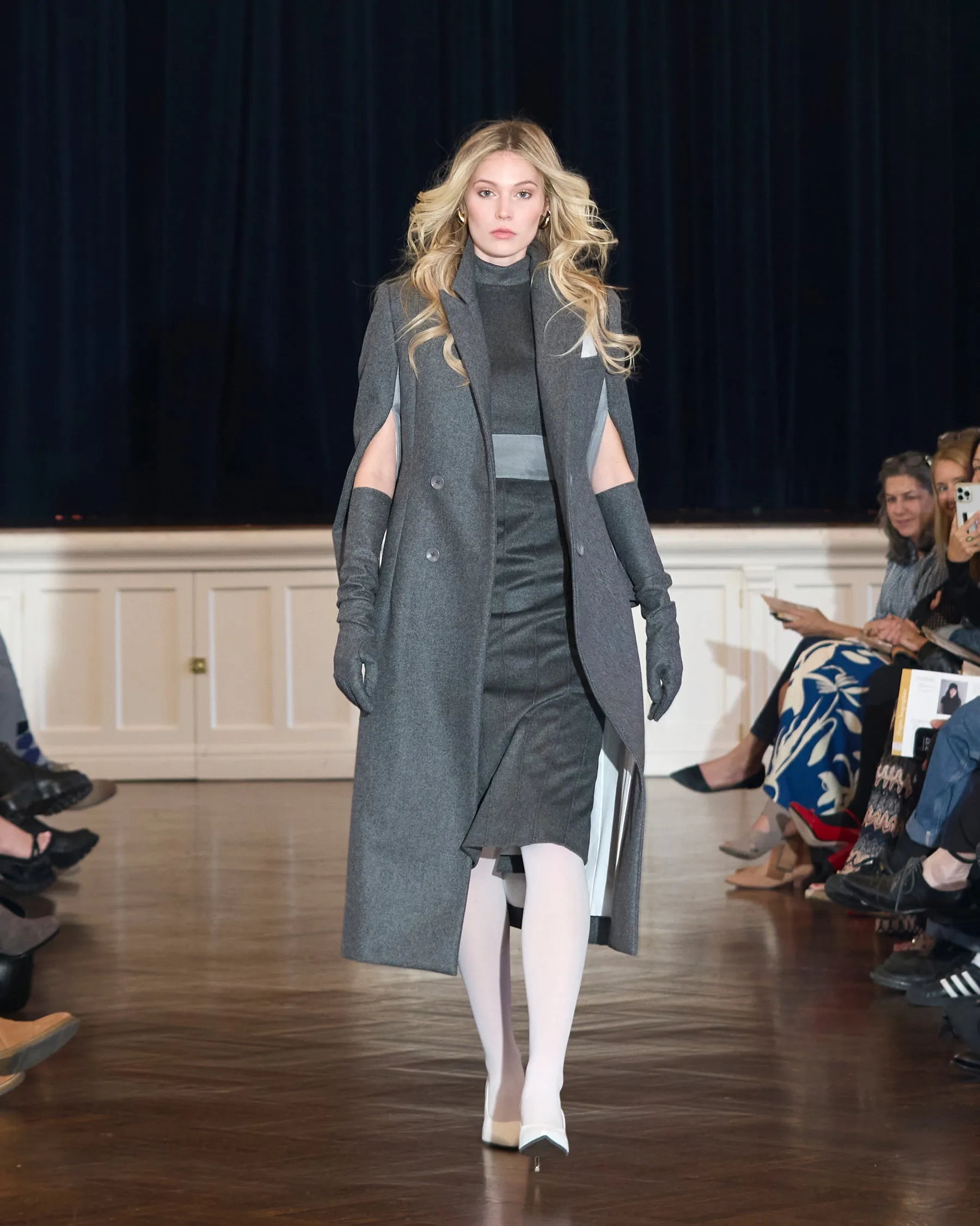 A model in a long grey coat on the runway at Threaded Stories