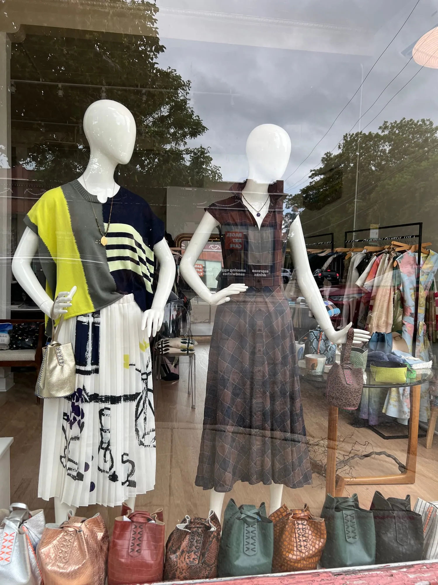 Two dressed mannequins in the cloth + home window, photographed from the sidewalk