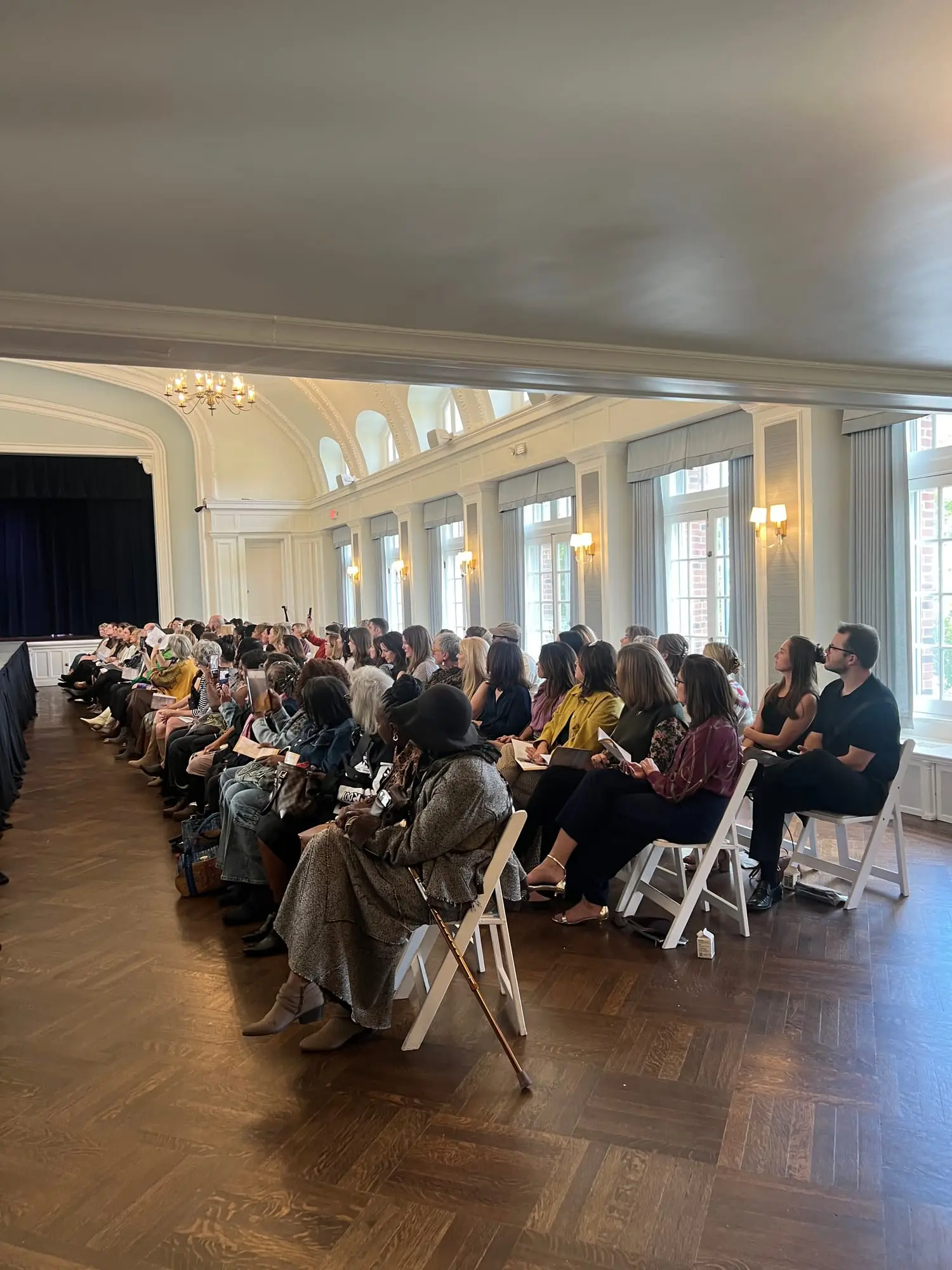 A full house at Threaded Stories — guests seated in rows along the runway in the ballroom of The Woman's Club of Evanston, the stage at the far end and tall arched windows down one side