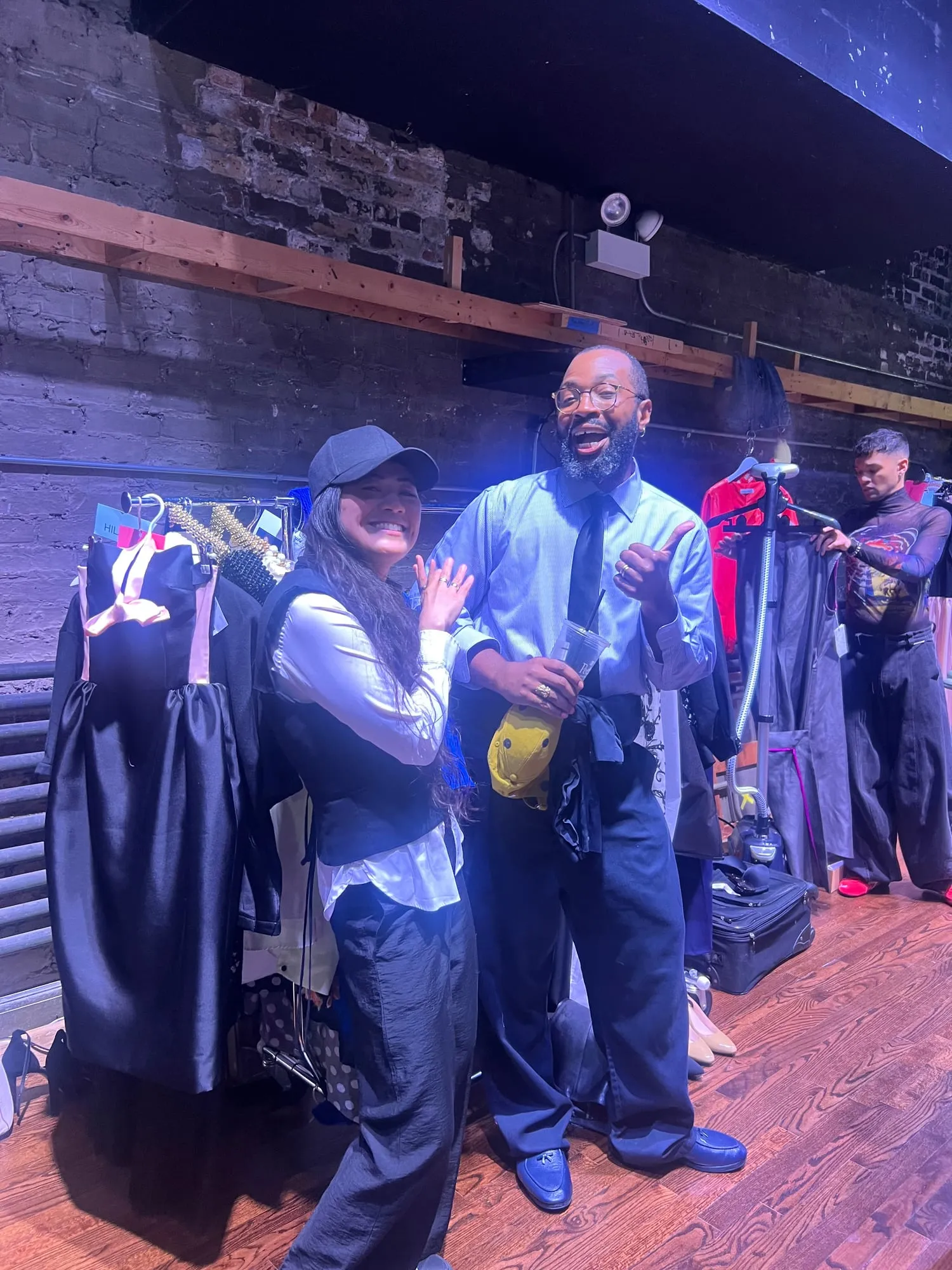 Backstage under a blue wash — racks, garment bags and the crew before the show