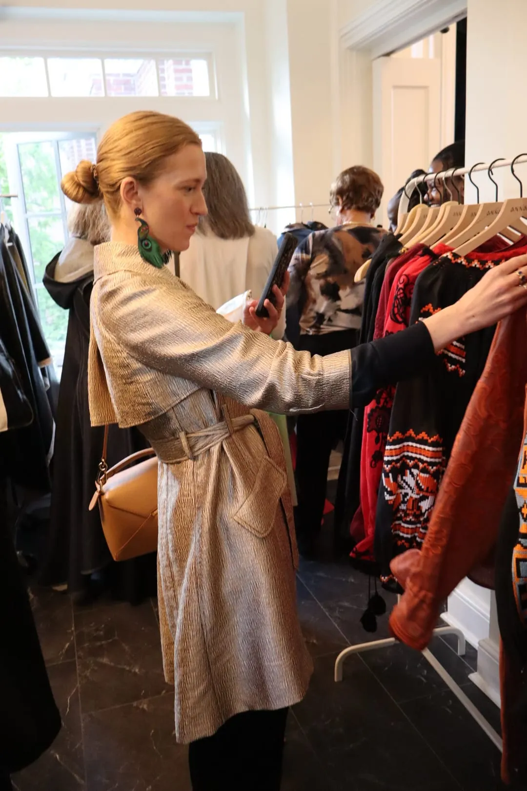 A guest in a gold trench coat looking through a rack of coats at the venue