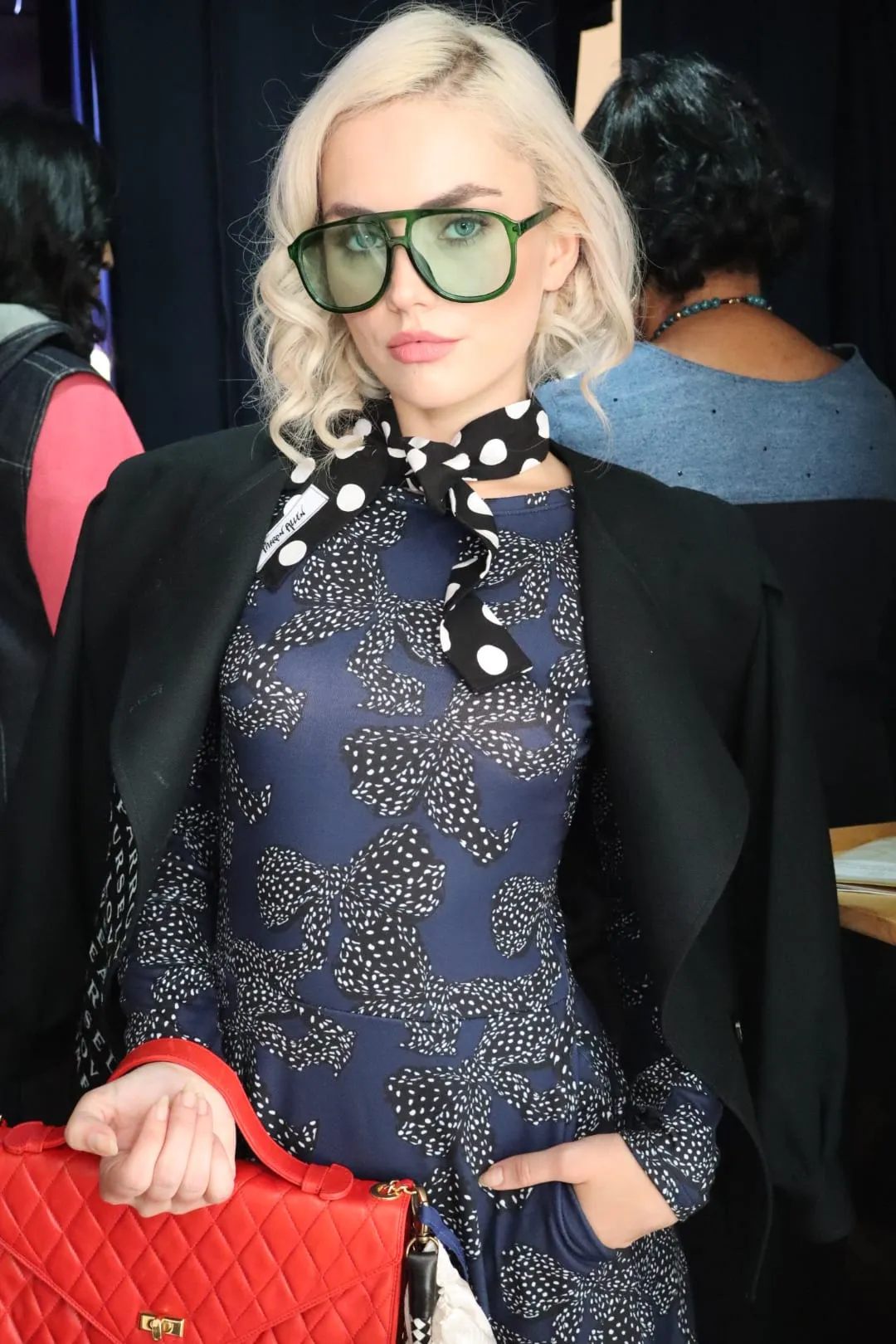 A guest in green glasses wearing the navy print look off the runway, holding the red bag