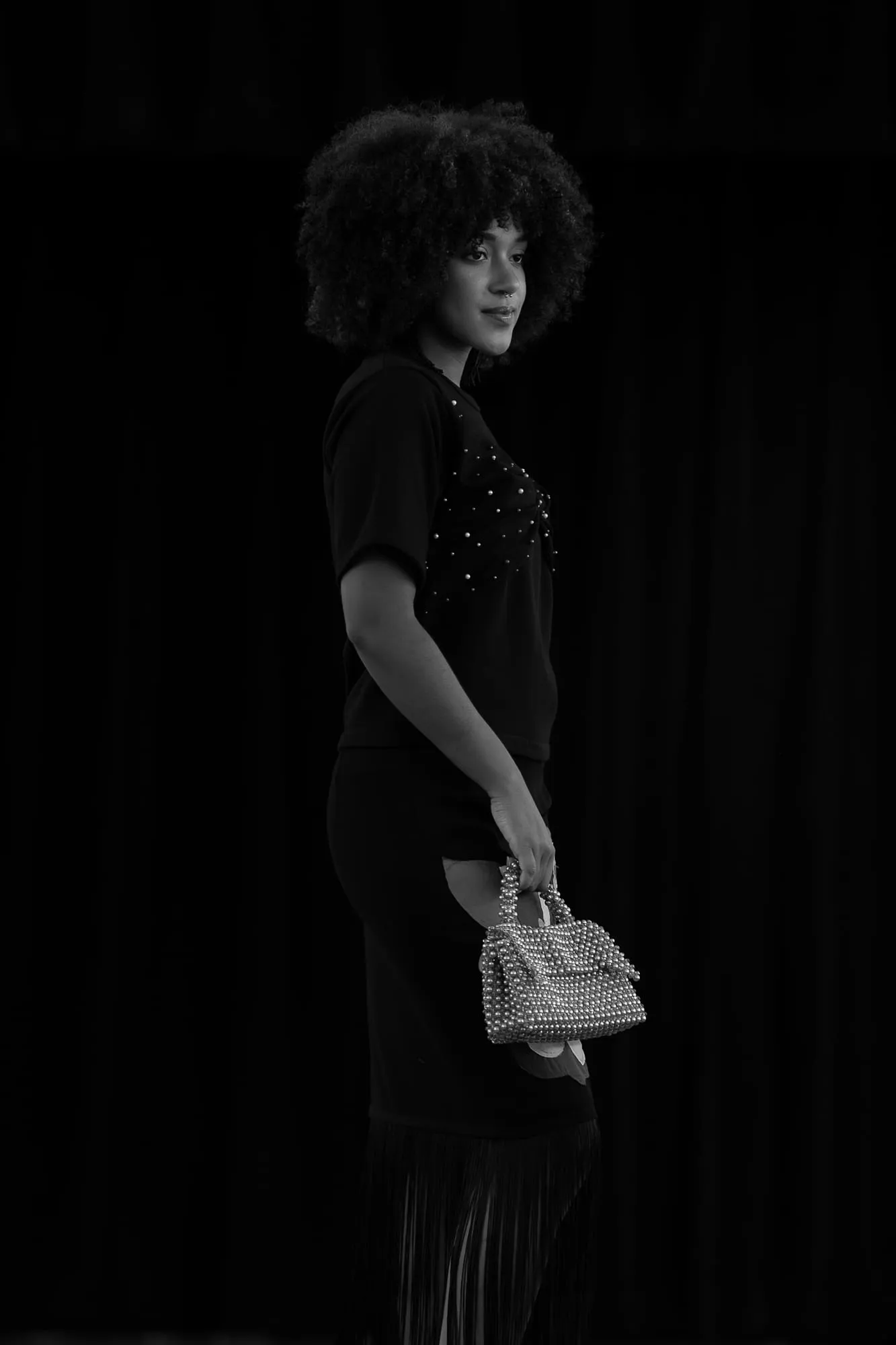 A model on the Threaded Stories runway in black, carrying a beaded bag — in black and white
